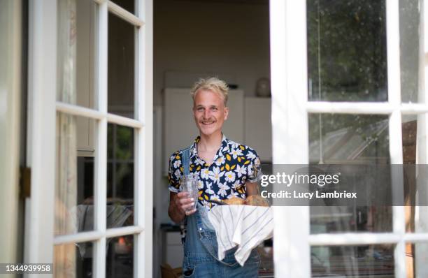 non-binary person leaving the kitchen carrying a bread basket and drinking glasses - sunny kitchen stock pictures, royalty-free photos & images