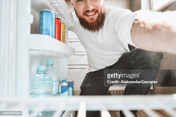 smiling male opening fridge to take out groceries at home - opening night of bright star arrivals stockfoto's en -beelden