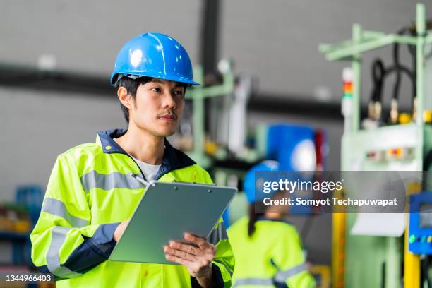 asian male technician industrial engineer in the hard hat safty uniform checking date machine operation while standing in front of in the heavy industry manufacturing factory industrial concept - civil engineering stock pictures, royalty-free photos & images