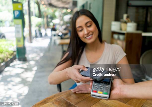 woman at a restaurant making a contactless payment with her cell phone - mobile payment stock pictures, royalty-free photos & images