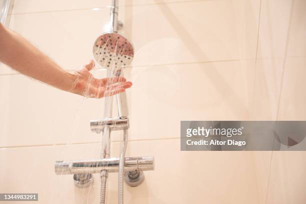 a man puts his arm under the shower water. - shower stock pictures, royalty-free photos & images