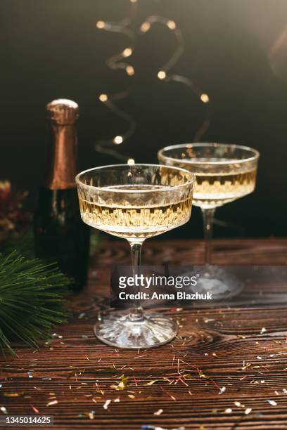 new year greeting card. champagne vintage glasses and bottle decorated with christmas decorations, pine, lights and confetti over dark wood background - christmas decorations stockfoto's en -beelden