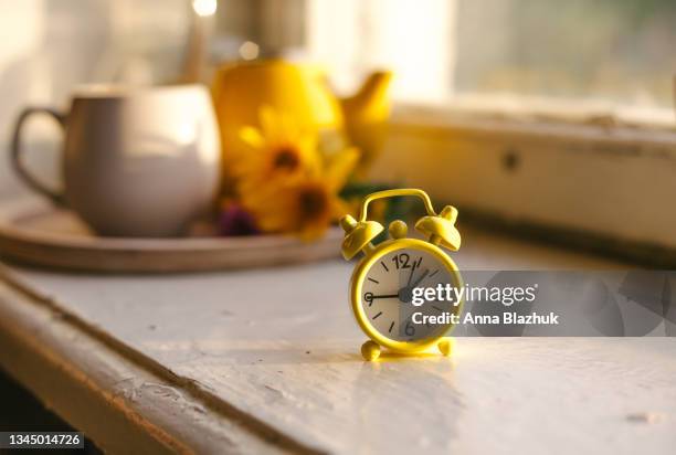 fall seasonal still life. retro alarm clock. fall back concept. cup with autumn flowers and kettle on wooden tray on window sill - daylight saving time 2021 stock pictures, royalty-free photos & images