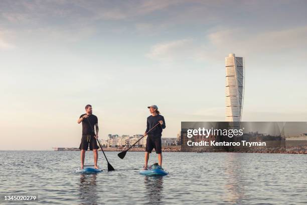 man talking with male instructor while paddleboarding in sea - malmö stock pictures, royalty-free photos & images