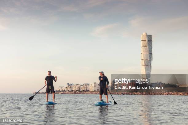 male friends paddleboarding against sky in sea - malmo sweden stock pictures, royalty-free photos & images