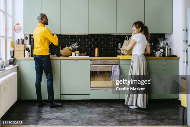 full length of smiling couple talking with each other while doing chores in kitchen at home - frau putzen stock-fotos und bilder
