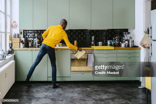 full length of mid adult man doing chores in kitchen at home - clean home stock pictures, royalty-free photos & images