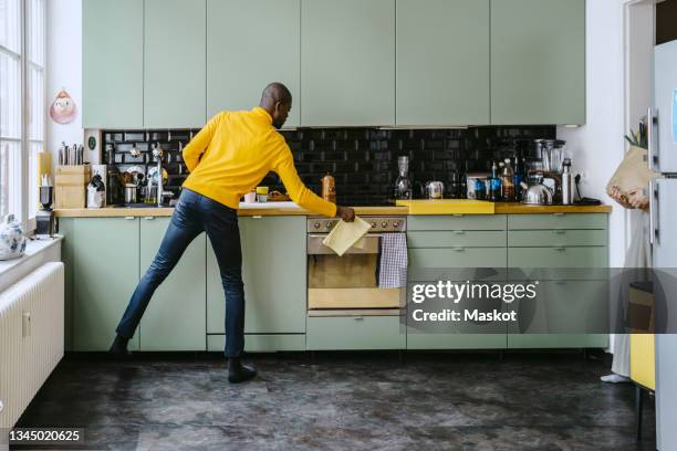 full length of mid adult man doing chores in kitchen at home - black man full length stock pictures, royalty-free photos & images