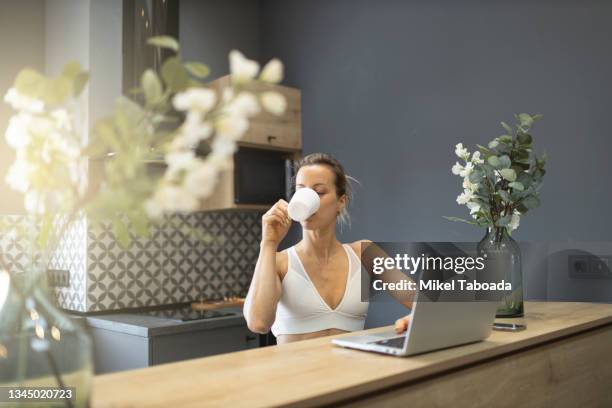 woman drinking coffee and using laptop in kitchen - ブラジャー ストックフォトと画像