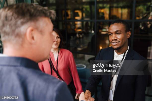 male professional greeting mature businessman with handshake during seminar at convention center - congress meeting stock pictures, royalty-free photos & images