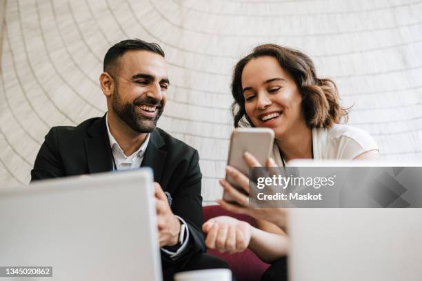 cheerful male and female professionals discussing over smart phone while sitting together during networking event - congress meeting stock pictures, royalty-free photos & images