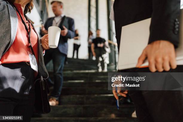 mature businesswoman holding coffee mug while discussing with male colleague during networking event - congress stock-fotos und bilder