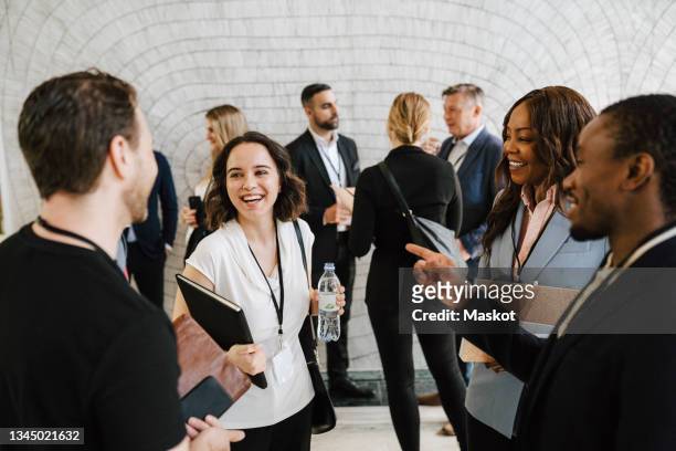 cheerful businesswoman discussing with male and female professional while standing together at convention center - kongressversammlung stock-fotos und bilder