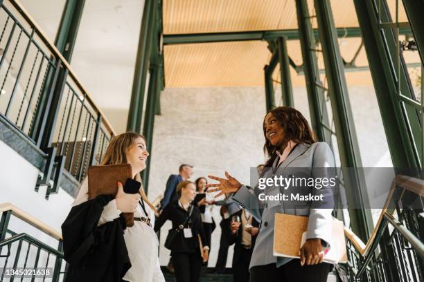 female professional gesturing while discussing with pregnant businesswoman on stairs at convention center - congress meeting stock pictures, royalty-free photos & images