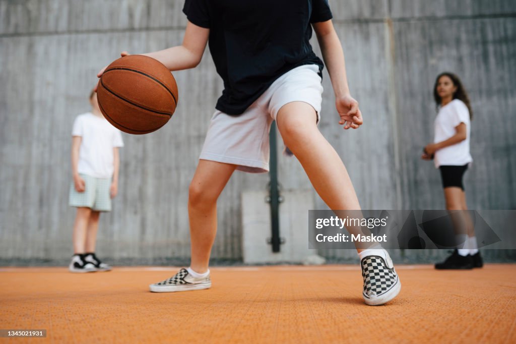 Low section of girl dribbling basketball while playing in court