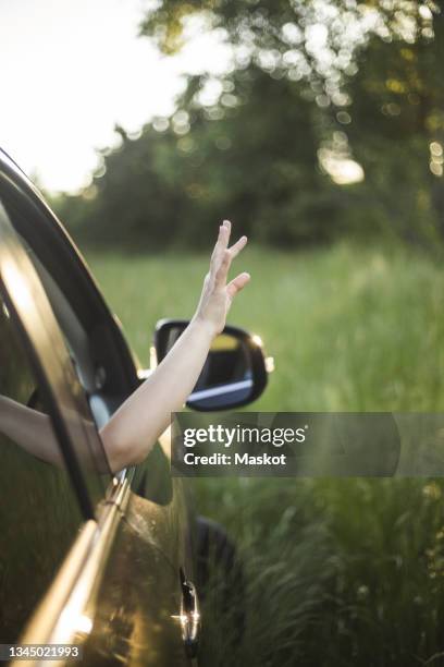 portrait of mother, father and two daughters standing by car at electric vehicle charging station - waving hand stockfoto's en -beelden