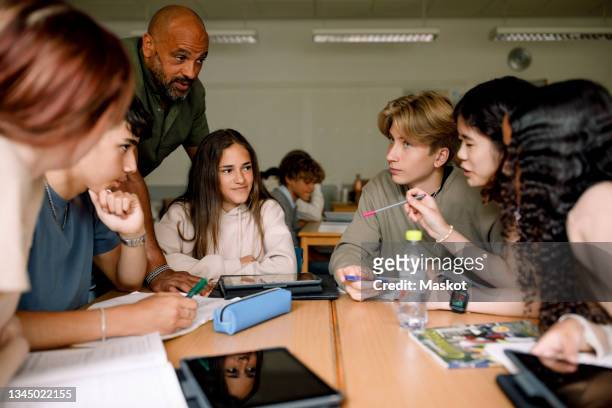 teenage girls and boys discussing with male teacher in classroom - group learning stockfoto's en -beelden
