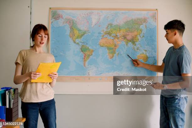 teenage girl reading while boy pointing on world map in classroom - students map imagens e fotografias de stock