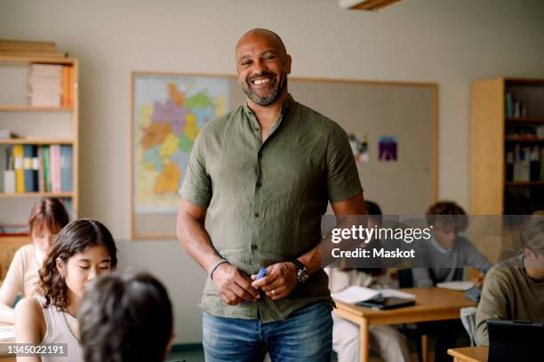 portrait of male teacher standing in classroom - teachers imagens e fotografias de stock