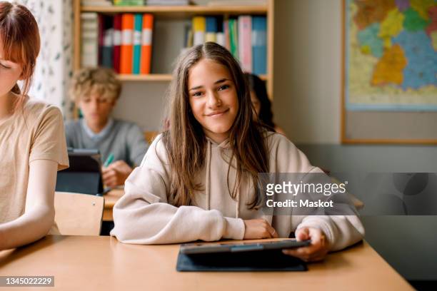 smiling girl holding digital tablet in classroom - ipad studying stock pictures, royalty-free photos & images