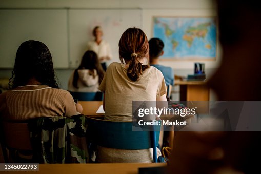 Rear view of teenage girls and boys learning in classroom Rear view of teenage girls and boys learning in classroom