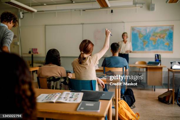 teenage girl raising hand in high school classroom - brugklas stockfoto's en -beelden