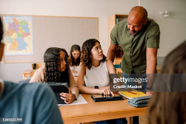 male teacher teaching teenage girls over digital tablet at desk in classroom - male teen tablet stock-fotos und bilder