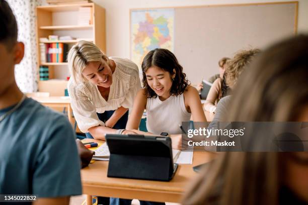 smiling teacher teaching girl studying on digital tablet in classroom - brugklas stockfoto's en -beelden