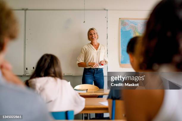 smiling female professor teaching students in classroom at high school - teacher classroom stock-fotos und bilder
