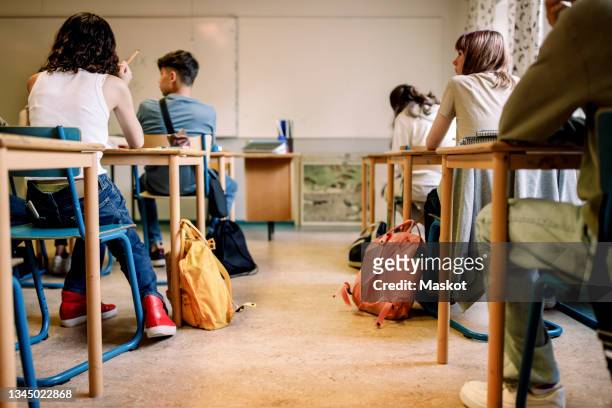 multiracial group of students sitting at desk in classroom - class photos et images de collection