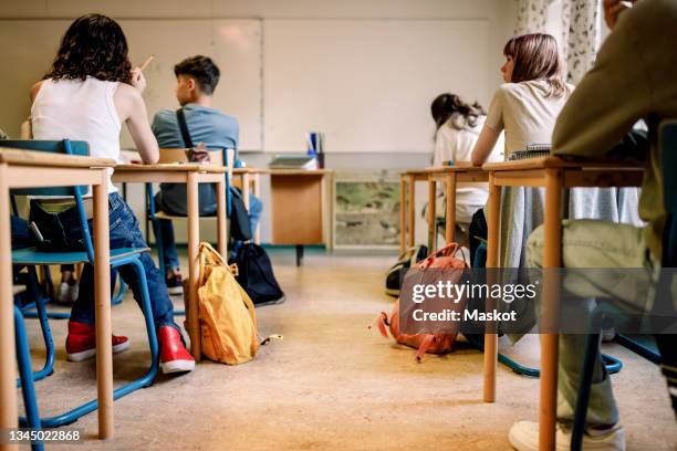 multiracial group of students sitting at desk in classroom - class imagens e fotografias de stock