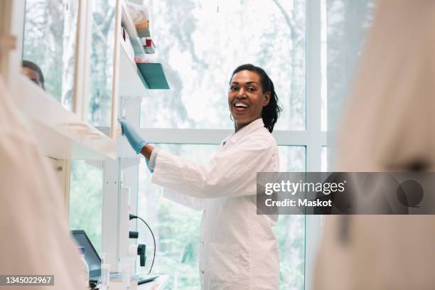 happy female medical expert looking away while working in laboratory - microbiologist stock pictures, royalty-free photos & images