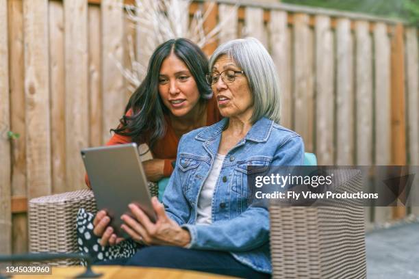 mujer mayor aprendiendo a usar la tableta con la ayuda de su hija adulta - hijo adulto fotografías e imágenes de stock