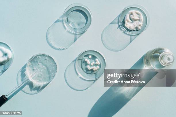 glass bottle with pipette near five petri dishes with creams, gel, face serum and tonic with pearls on light blue background. concept of cosmetics laboratory researches. photography in flat lay style - dropper bottle stock pictures, royalty-free photos & images