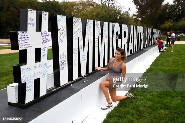 Visitors at the 92 ft long #IMMIGRANTSAREESSENTIAL art activation on the National Mall write messages of support to immigrant essential workers on...