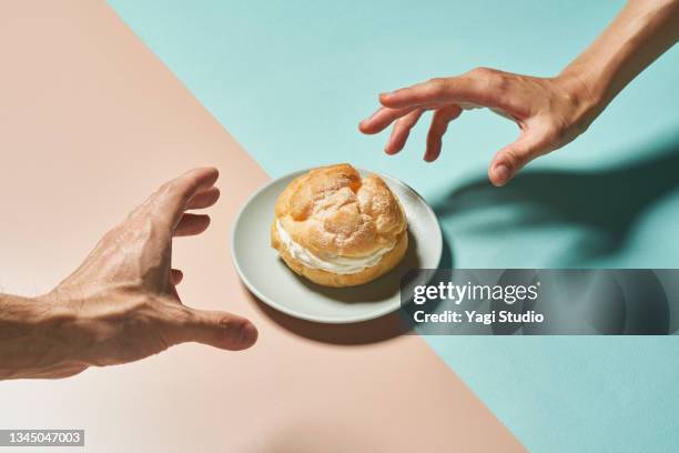cream puff and hands on a colorful background. - cremetorte stock-fotos und bilder