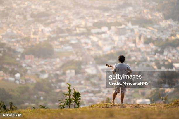 rear view of man playing guitar on the top of the mountain - street artist stock pictures, royalty-free photos & images