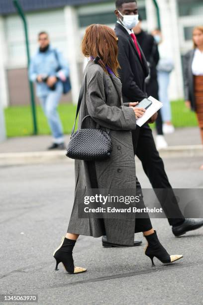 Christine Centenera wears black sunglasses, earrings, a gray checkered print pattern with purple collar long oversized coat, a black flowing high...