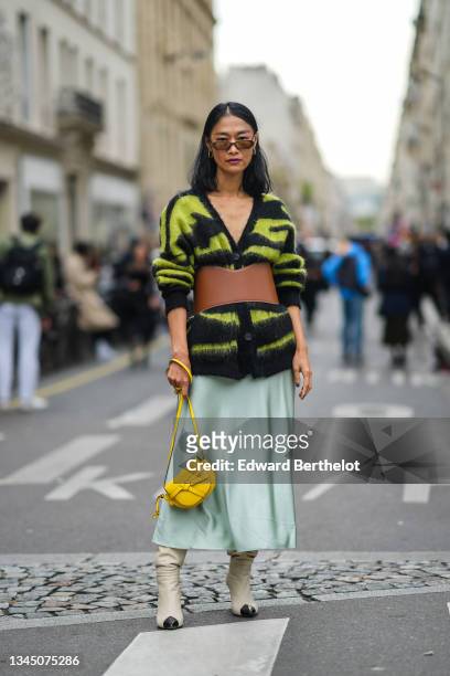 Pornwika Spiecker wears sunglasses, gold and green earrings, a black and green zebra print pattern fluffy long pullover, a brown shiny leather belt,...