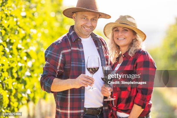 winemaking couple dressed in typical farming clothes, with glasses of wine in hands celebrates succesful harvest in vineyard. - fall harvest stock-fotos und bilder