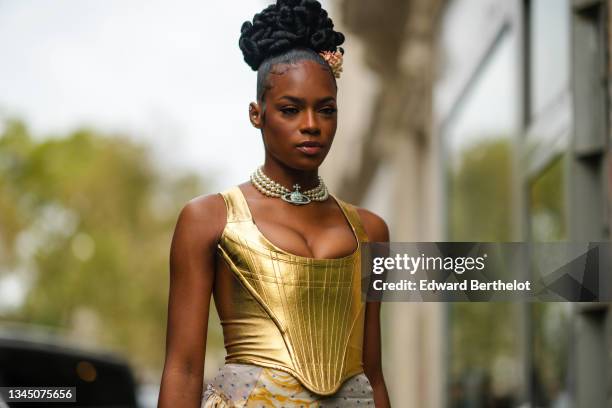 Didi Stone wears orange flower hair clip, earrings, a white pearls with silver Vivienne Westwood large logo necklace, a gold shiny leather V-neck...