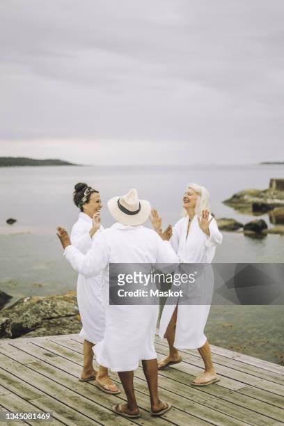 joyful senior women in bathrobe dancing on pier during vacation - morgonrock bildbanksfoton och bilder