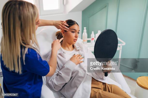 dermatologist prepares the patient for facial treatment while she looks herself in the mirror - dermatologists talking to each other patient stock pictures, royalty-free photos & images