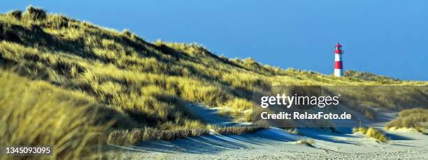 farol listrado vermelho e branco em dunas de areia na costa da ilha sylt, região do mar do norte alemão - german north sea region - fotografias e filmes do acervo
