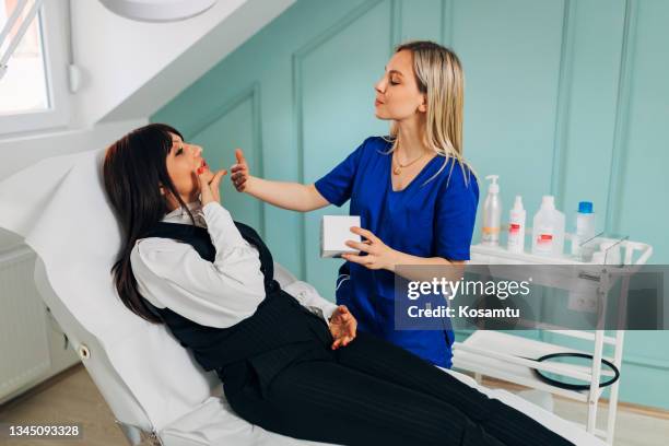 young beautician applies a face cream to the patient to give her skin a better glow - dermatologists talking to each other patient stock pictures, royalty-free photos & images