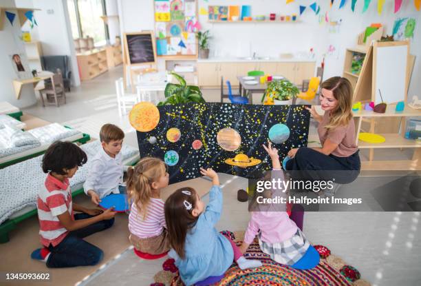 high angle view of pre school teacher showing poster with planets to children indoors in nursery, montessori education. - profesor fotografías e imágenes de stock