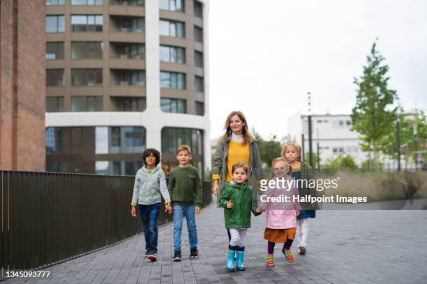 pre school teacher with multiracial group of small children on walk outdoors in town. - babysit stockfoto's en -beelden