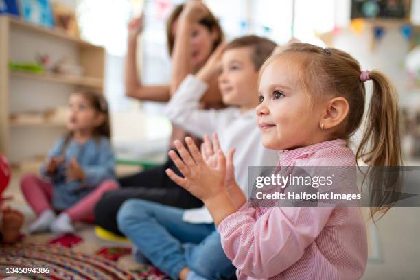 close up of happy pre school girl sitting on floor with group of children and teacher and clapping hands indoors in nursery. - teacher pre school bildbanksfoton och bilder