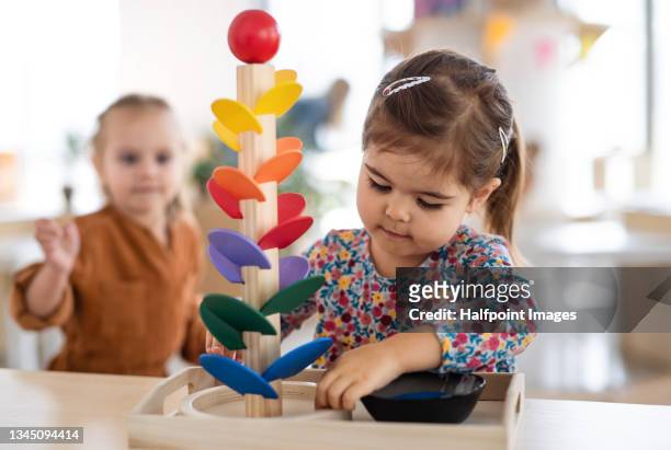 two pre-school girls playing with marble run indoors in nursery, montessori education. - toddler stock-fotos und bilder