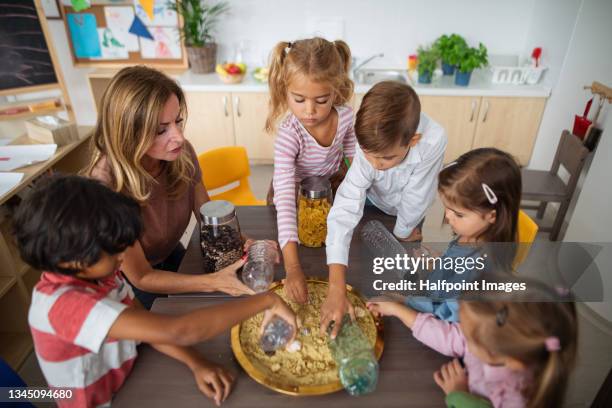 high angle view of pre school teacher with multiracial group of children sitting at table and playing indoors in nursery, montessori education. - モンテッソーリ教育 ストックフォトと画像